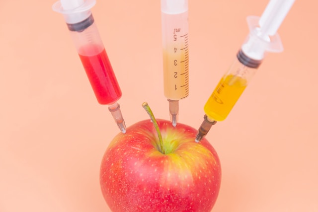 Three needles injecting different colored fluids into a red apple. Photo by Diana Polekhina on Unsplash