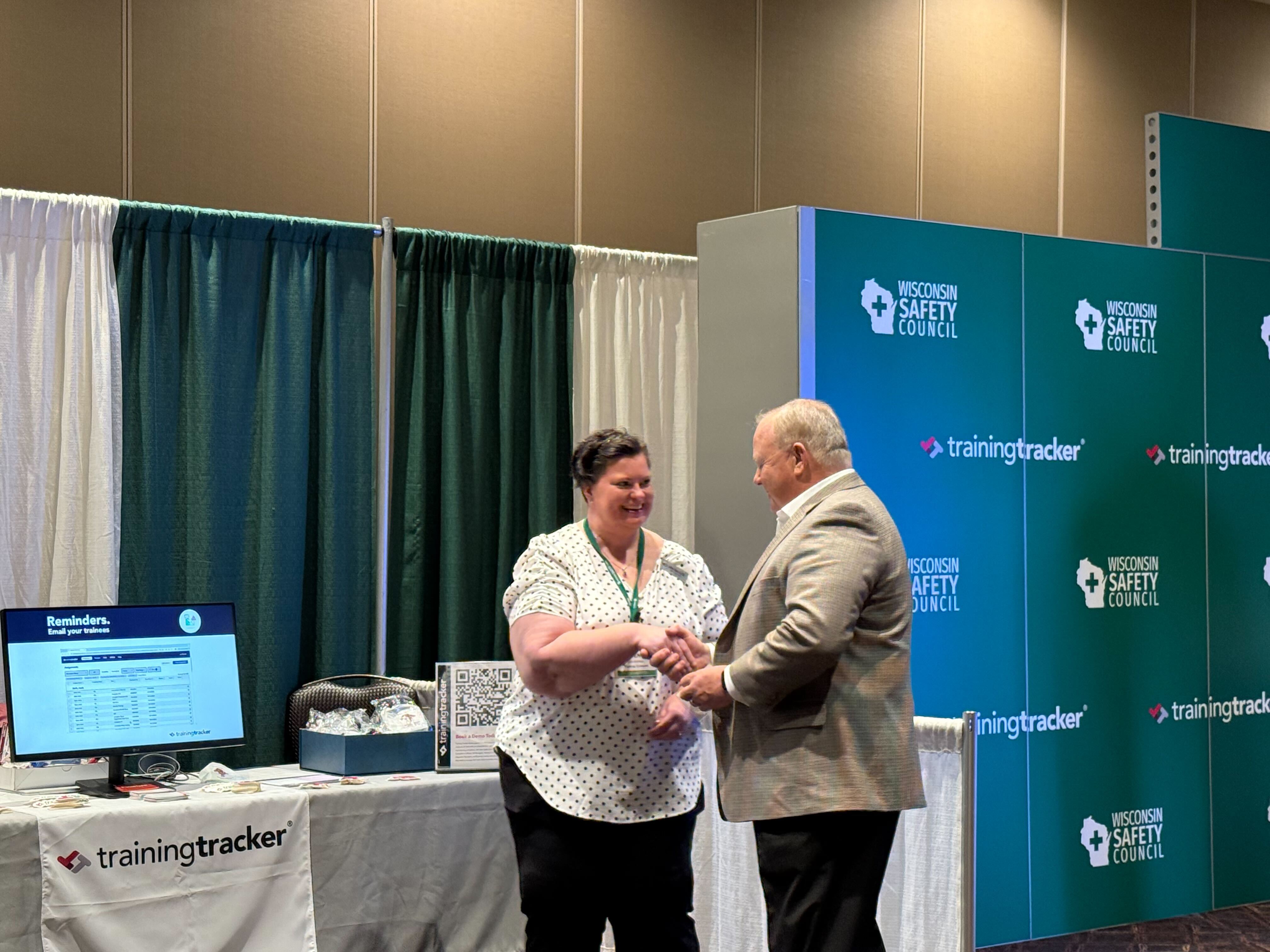 Woman in white blouse shaking hands with older man in suit at a professional event with blue backdrop.