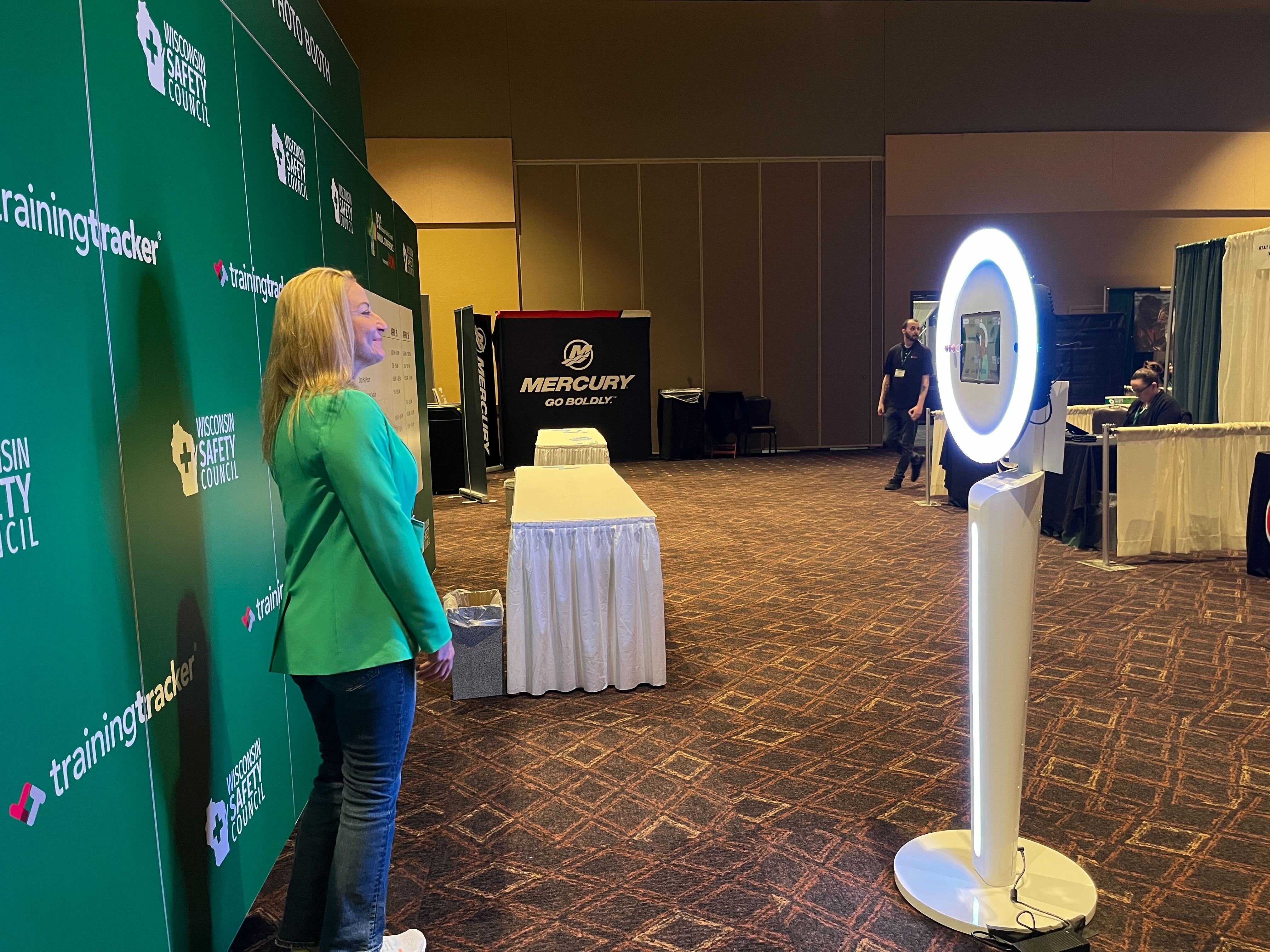 Woman in green blazer at Wisconsin Safety Council exhibition booth viewing a ring light photo station.