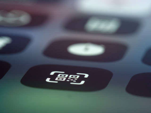 QR code icon on smartphone screen with other apps visible in blurred background.
